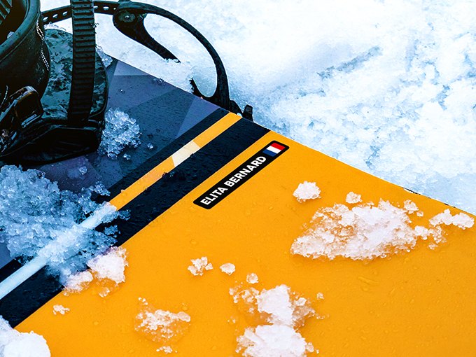 Zwarte naamsticker met Franse vlag op een geel snowboard in de sneeuw