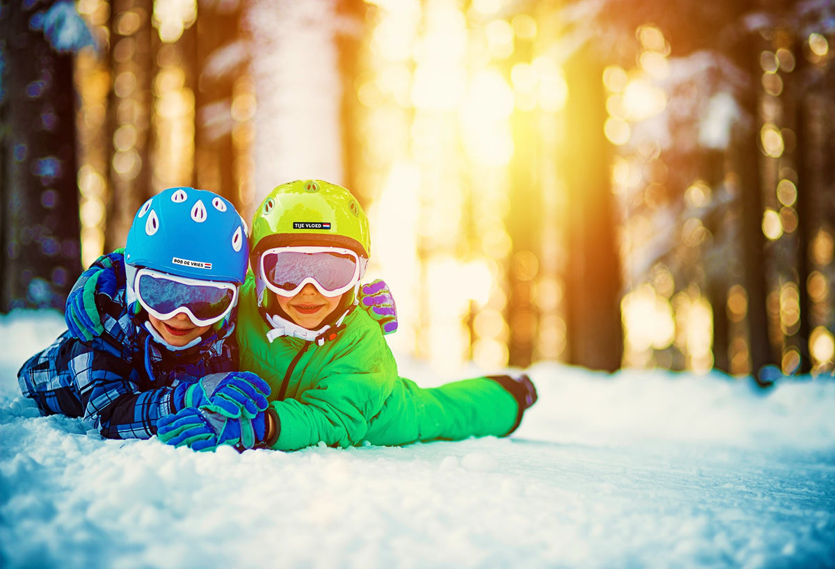 Twee kinderen in de sneeuw met een naamsticker op hun skihelm